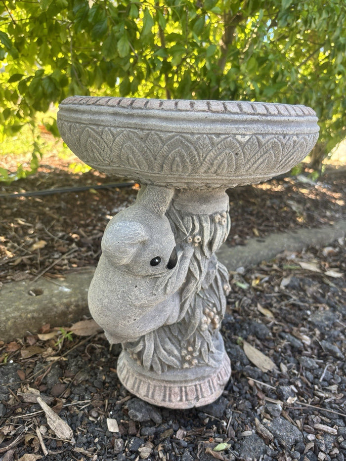 concrete bird bath featuring a sculpted koala on a textured tree trunk base in a garden