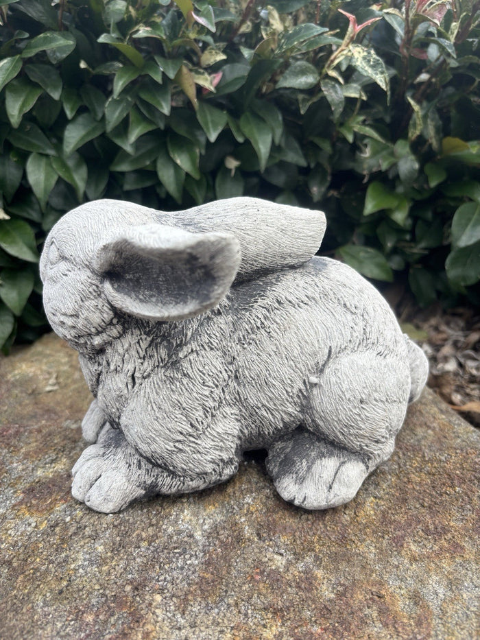 handcrafted grey concrete rabbit statue with realistic fur texture in a garden setting