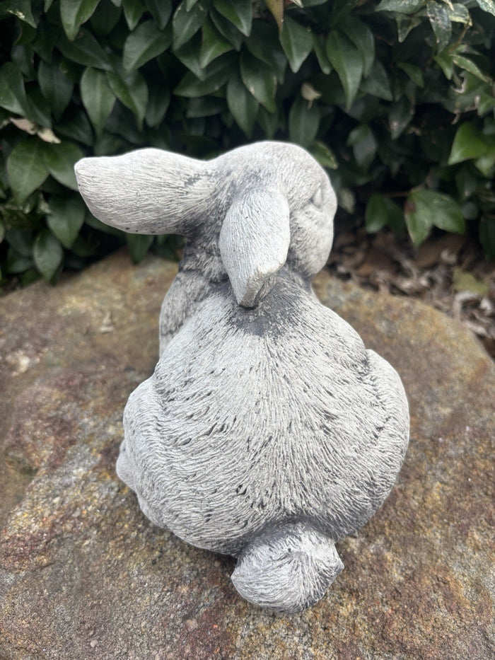 grey concrete rabbit sculpture with realistic fur texture sitting on a stone garden path