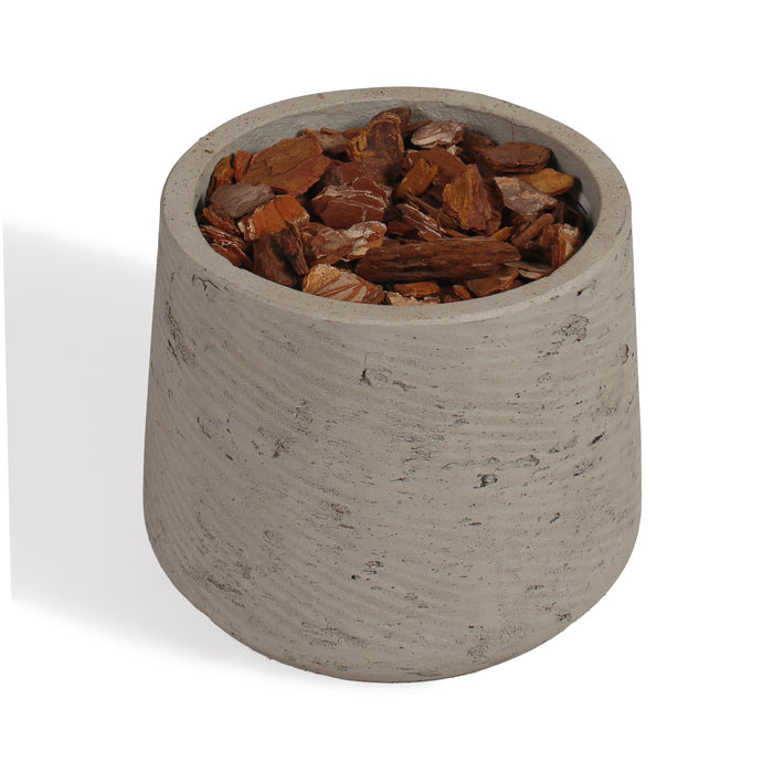 A small cylindrical concrete planter with a textured light gray finish, filled with chunky brown bark chips, shown on a white background.