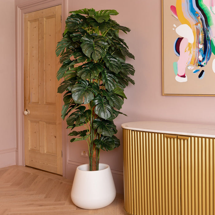 Modern interior with a gold cabinet, potted plant, and colorful abstract art on a pink wall.