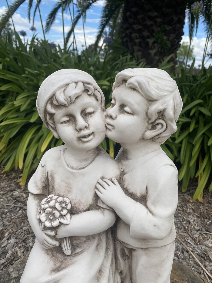 22nice4me Garden Statues antique white fibre clay sculpture of two children kissing, holding a bouquet of flowers.