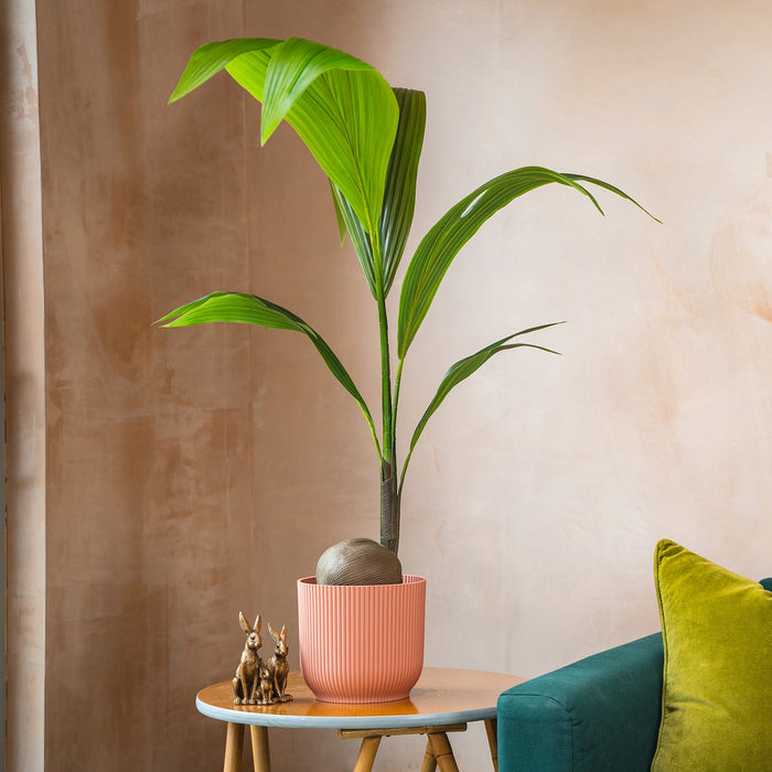Green plant on a small table next to a teal sofa with colorful cushions against a beige wall.