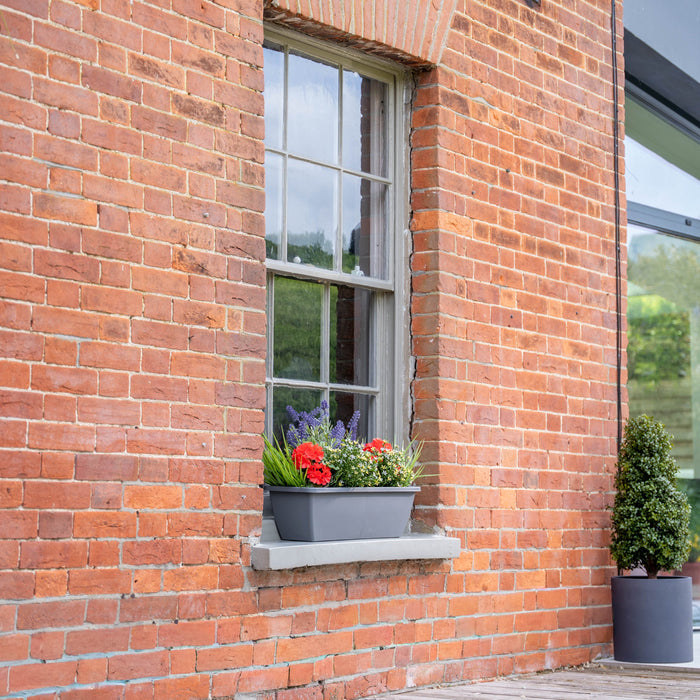 Brick building with a colourful window box on a grey windowsill.