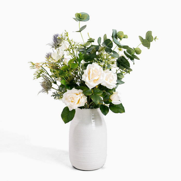 Bouquet of white flowers and greenery in a white vase on a white background