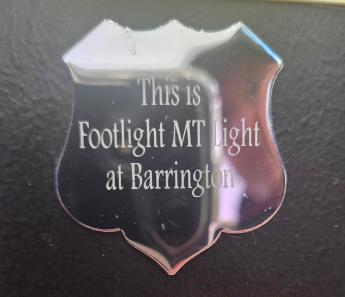 Silver shield-shaped plaque with engraved text on black background, close-up view