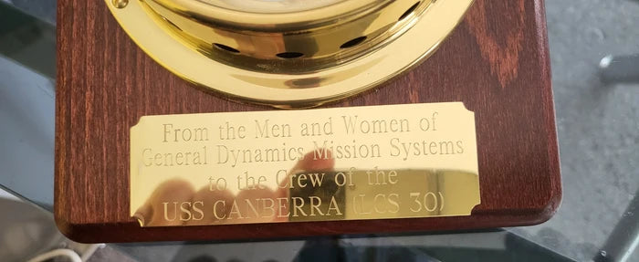Engraved brass plaque on wood honoring USS Canberra LCS 30, nautical instrument setting