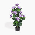 An artificial hydrangea plant with purple flowers and green leaves, potted in a black plastic pot, shown against a plain white background.
