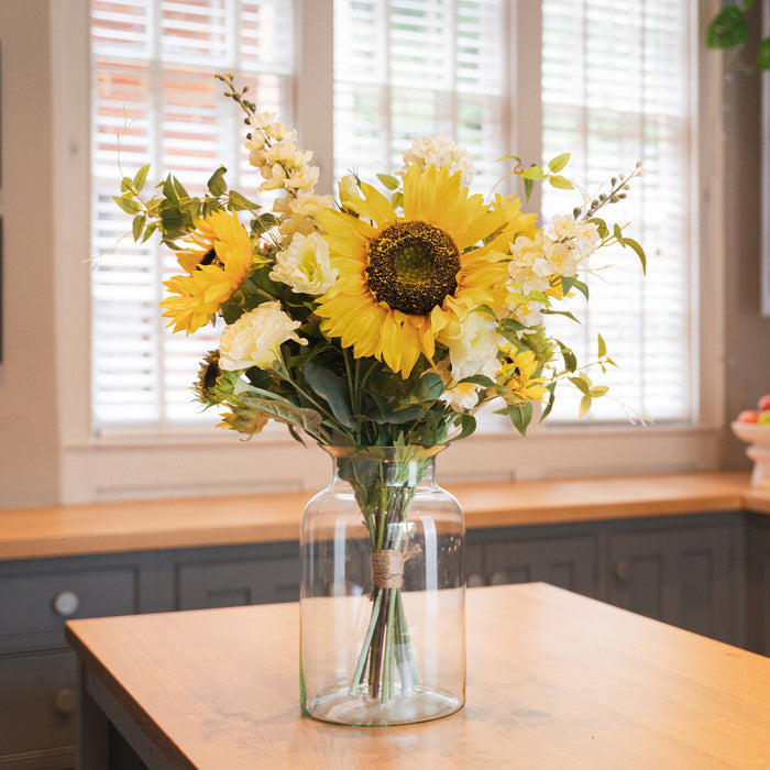 Bouquet of sunflowers and white flowers in a clear vase on a kitchen counter.