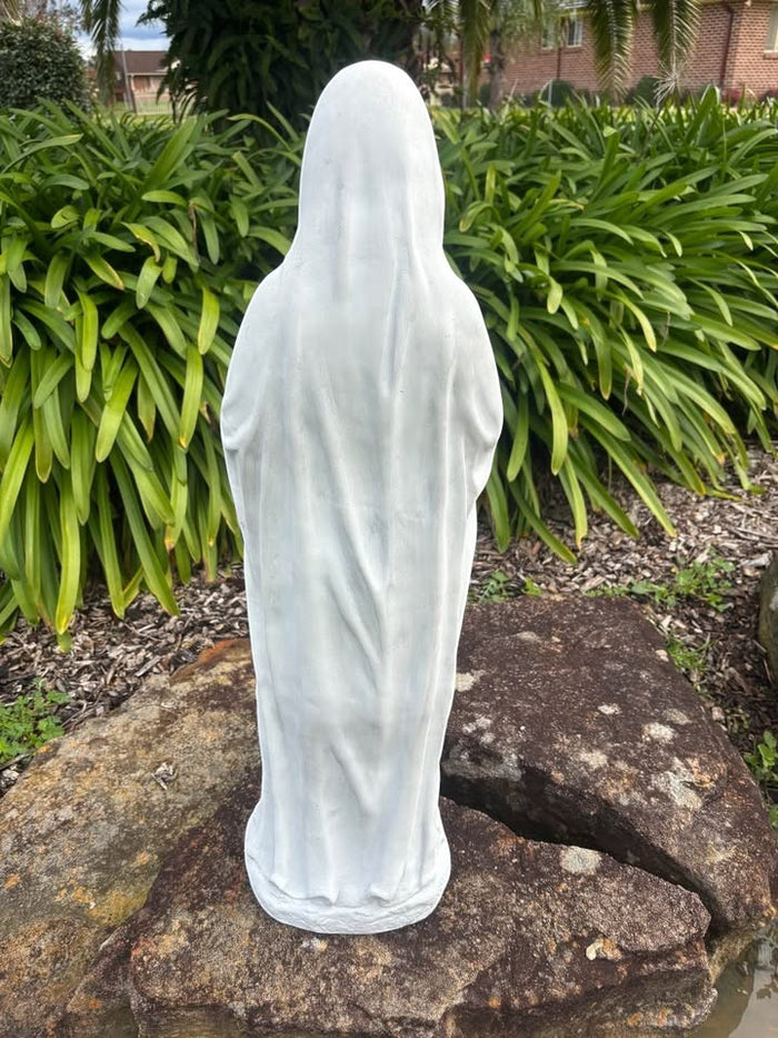 Back view of a 22nice4me Garden Statues resin Virgin Mary statue standing on a rock in a lush outdoor garden.