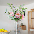 Clear vase with pink flowers and green leaves on a kitchen counter.