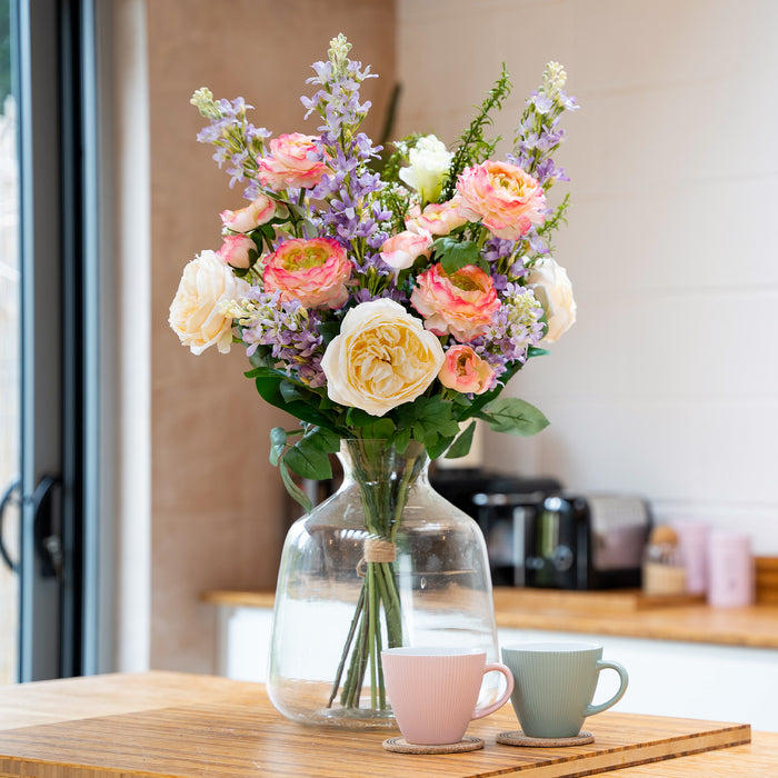 Bouquet of flowers in a clear vase on a table with two cups in a kitchen setting.