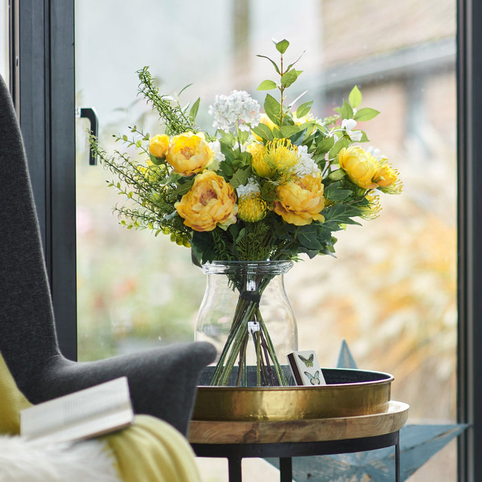 Bouquet of yellow flowers in a clear vase on a small round table with a star decoration, in front of a glass door.