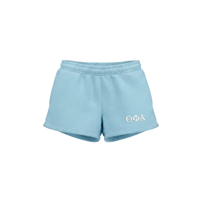 Light blue athletic shorts with a white embroidered Greek letter logo 'THETA PHI ALPHA' on the lower left leg, shown against a plain white background.